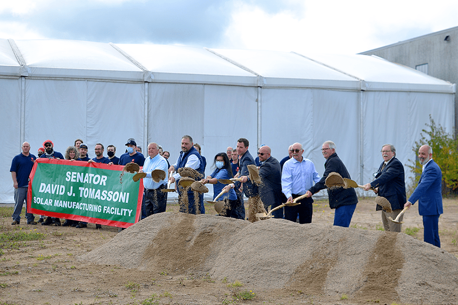 A group of people shovel a pile of dirt in a groundbreaking ceremony for a major solar panel factory expansion